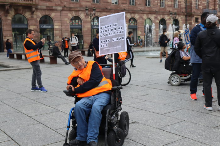 Photo d'un manifestant portant le message "Quand on aime, on ne compte pas. Avec l’AAH, si !” AFP France handicap"